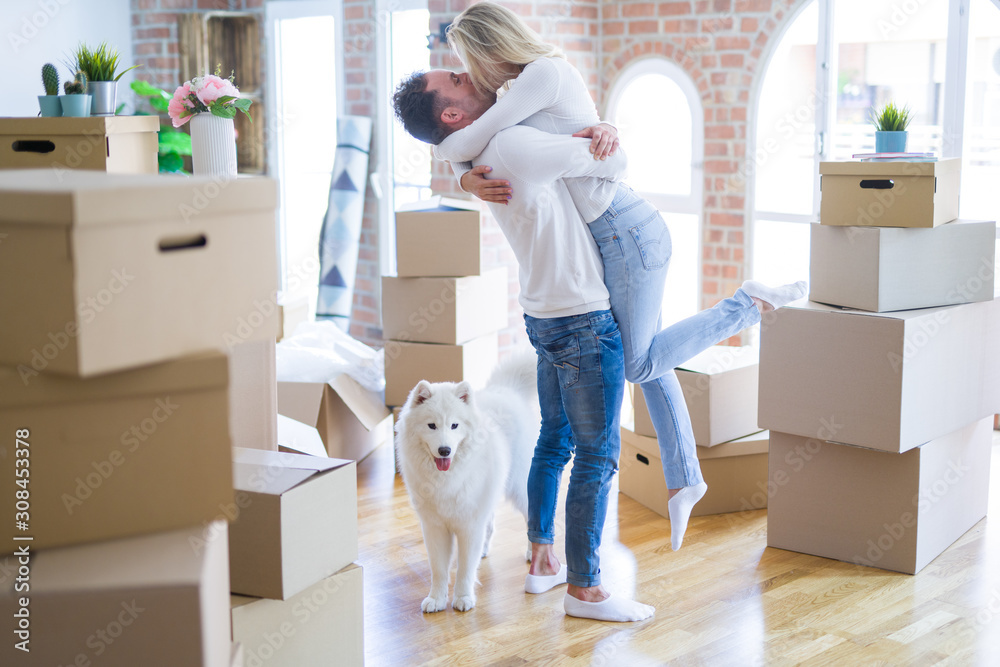 Fototapeta premium Young beautiful couple with dog hugging at new home around cardboard boxes