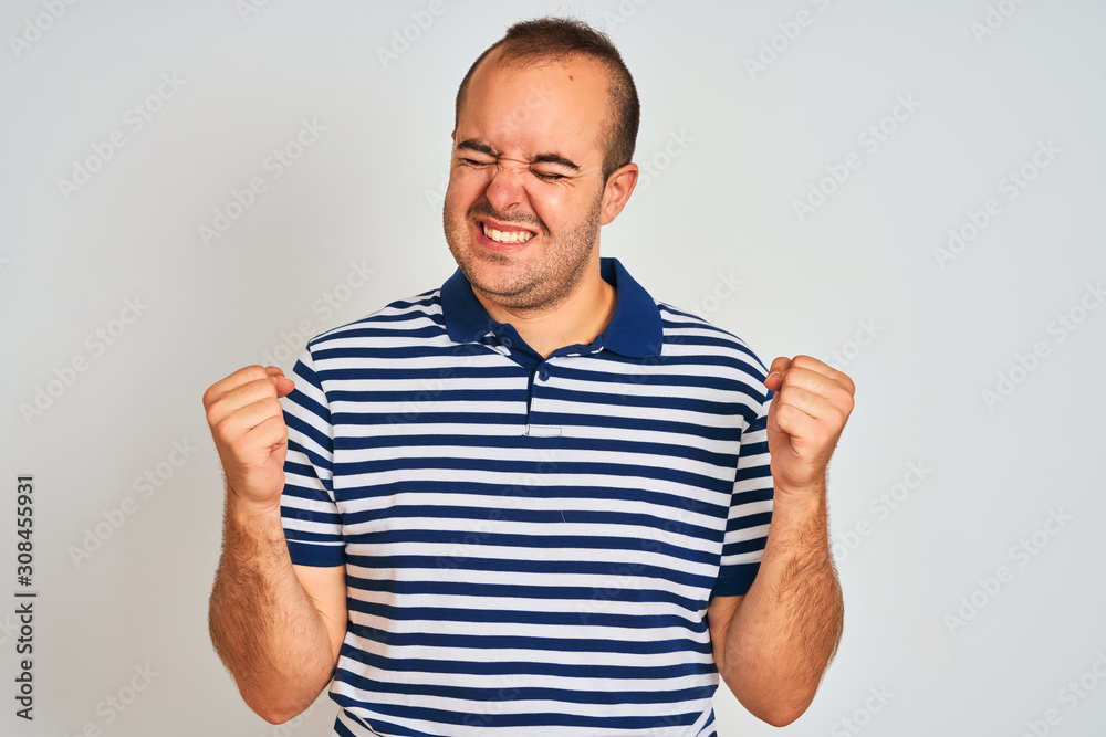 Young man wearing casual striped polo standing over isolated white background very happy and excited doing winner gesture with arms raised, smiling and screaming for success. Celebration concept. Young man wearing casual striped polo standing over isolated white background very happy and excited doing winner gesture with arms raised, smiling and screaming for success. Celebration concept.
