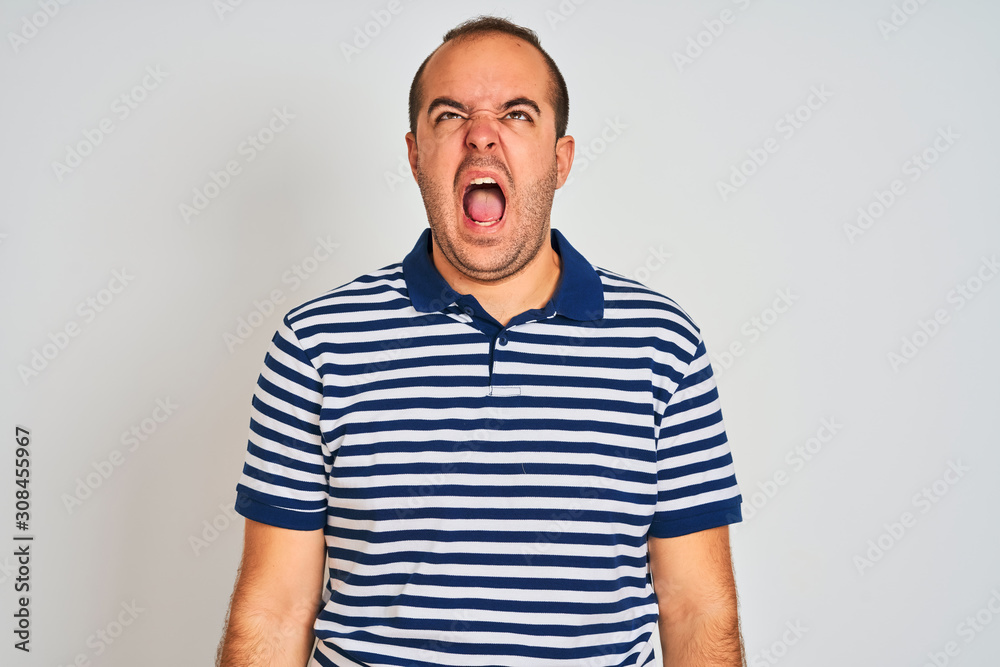 Young man wearing casual striped polo standing over isolated white background angry and mad screaming frustrated and furious, shouting with anger. Rage and aggressive concept. Young man wearing casual striped polo standing over isolated white background angry and mad screaming frustrated and furious, shouting with anger. Rage and aggressive concept.