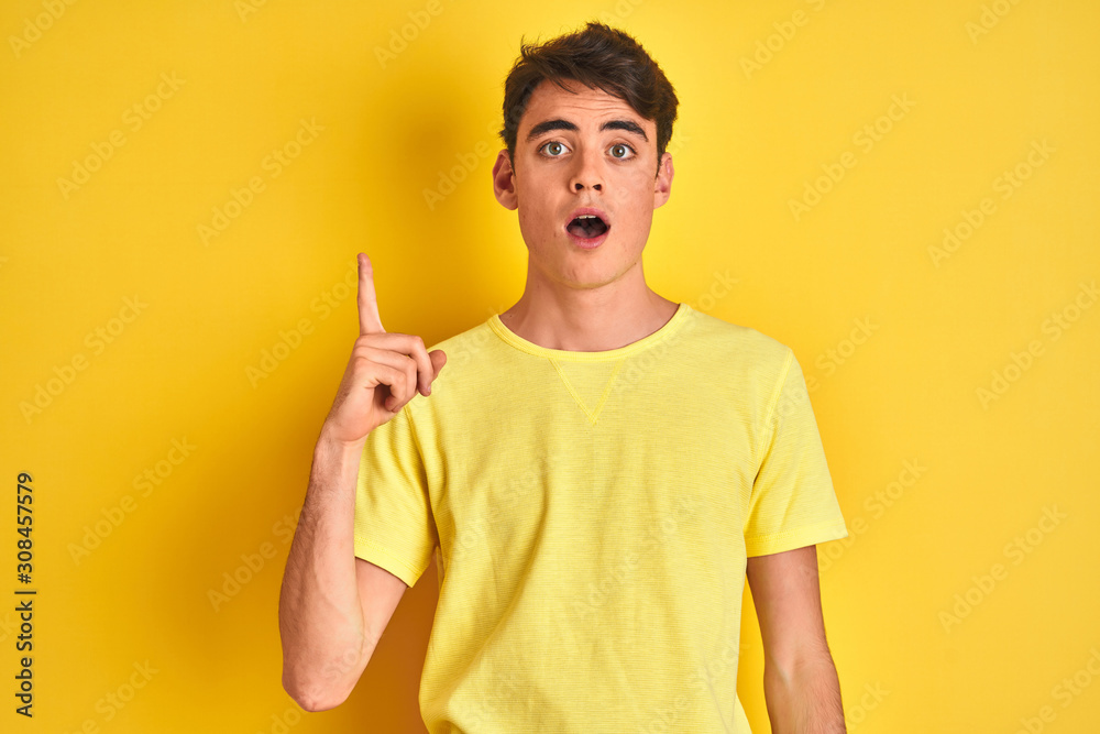 Teenager boy wearing yellow t-shirt over isolated background pointing finger up with successful idea. Exited and happy. Number one. Teenager boy wearing yellow t-shirt over isolated background pointing finger up with successful idea. Exited and happy. Number one.