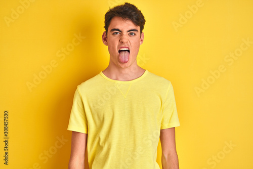 Teenager boy wearing yellow t-shirt over isolated background sticking tongue out happy with funny expression. Emotion concept.