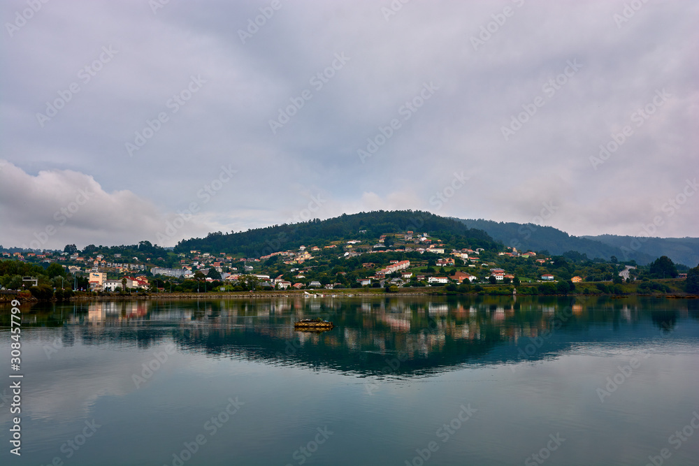 Houses on hill in northern Spain reflected in the water. Cloudy sky.