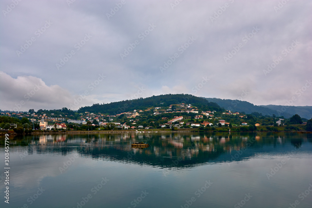 Houses on hill in northern Spain reflected in the water. Cloudy sky. Houses on hill in northern Spain reflected in the water. Cloudy sky.