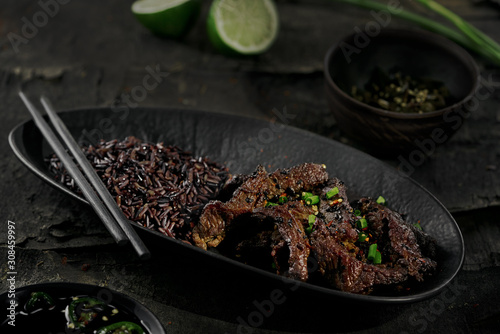 Chinese black pepper beef stir fry with black rice in a black clay plate on an old rustic table. © Maxim Khytra