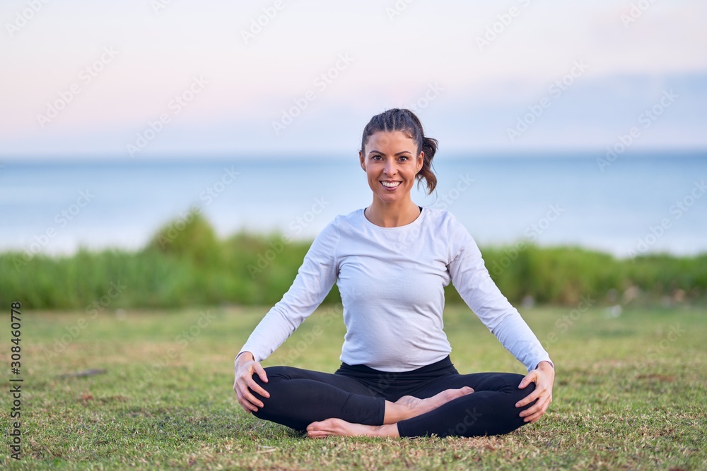 Young beautiful sportwoman smiling happy practicing yoga. Coach sitting with smile on face teaching lotus pose at park