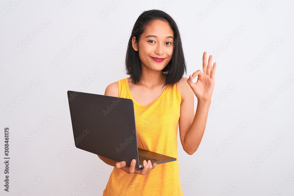 Young beautiful chinese woman using laptop standing over isolated white background doing ok sign with fingers, excellent symbol Young beautiful chinese woman using laptop standing over isolated white background doing ok sign with fingers, excellent symbol