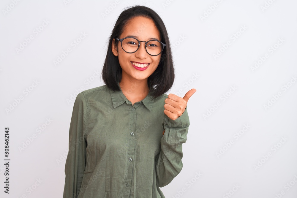 Young chinese woman wearing green shirt and glasses over isolated white background doing happy thumbs up gesture with hand. Approving expression looking at the camera with showing success. Young chinese woman wearing green shirt and glasses over isolated white background doing happy thumbs up gesture with hand. Approving expression looking at the camera with showing success.