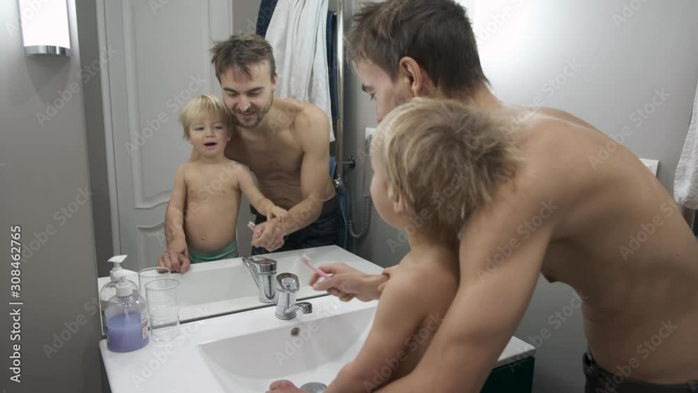 Father and his toddler son brush their teeth together in bathroom. Dad helps his little   child boy brush his teeth. Family morning routine. Tooth care for children. 