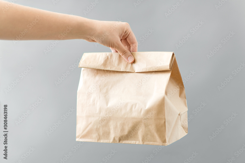 recycling and ecology concept - hand holding disposable brown takeaway food in paper bag with lunch on table - obrazy, fototapety, plakaty 