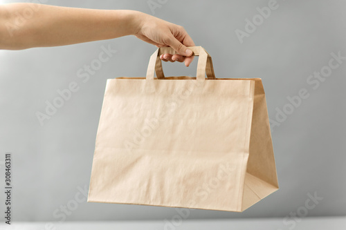 recycling, shopping and ecology concept - hand holding disposable brown takeaway food in paper bag with lunch on table photo