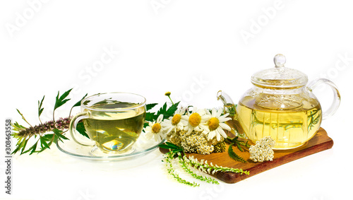 Herbal chamomile tea in a glass cup and teapot with fresh herbs(mother wort, chamomile, common yarrow) on cutting board isolated on white background