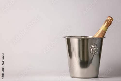 Bucket with bottle of champagne on light background