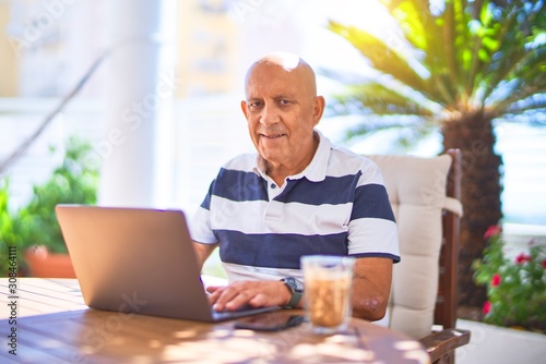 Senior handsome man smiling happy and confident. Sitting using laptop at terrace