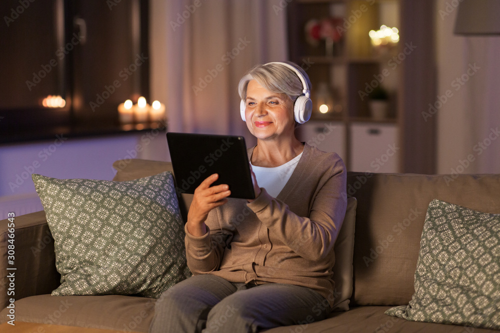 technology, people and lifestyle concept - happy senior woman in headphones and tablet pc computer listening to music at home in evening