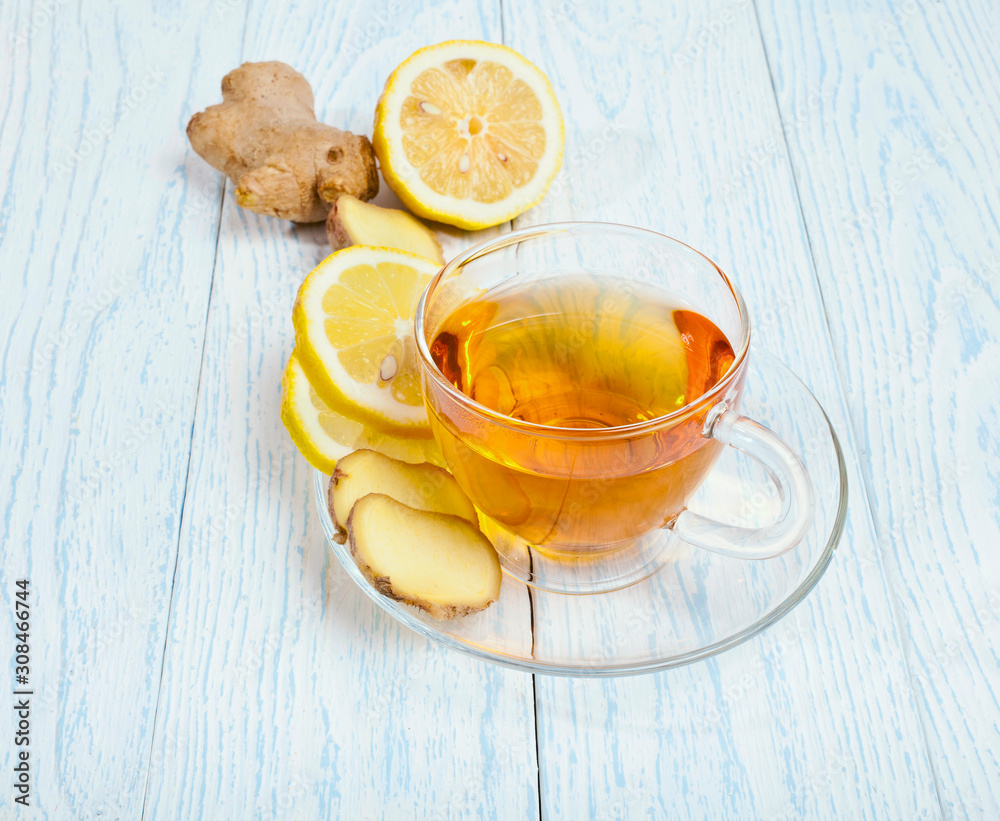 Glass cup of tea with ginger and lemon on a white wooden background.