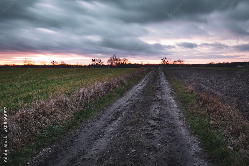 Dirt road through the fields and clouds in the sky after sunset
