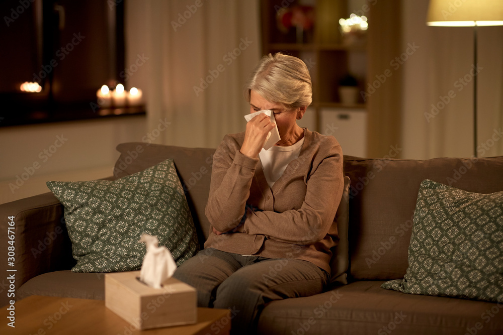 sadness, stress and people concept - unhappy crying senior woman wiping tears with paper tissue at home at night
