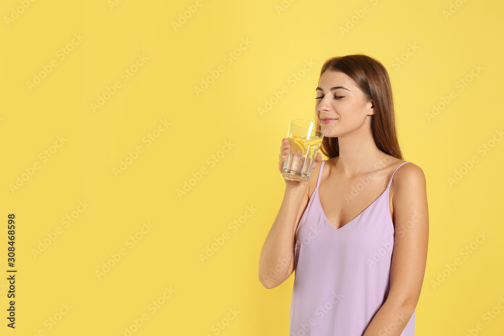 Young woman drinking lemon water on yellow background. Space for text Young woman drinking lemon water on yellow background. Space for text