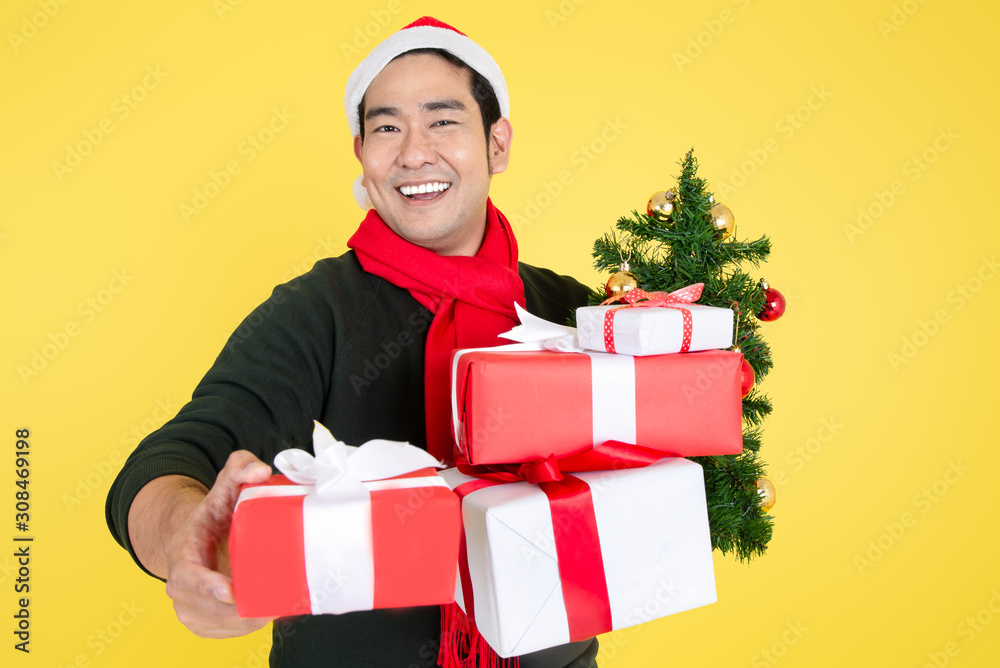 Happy Asian man wearing green sweater and Santa hat holding gift boxes on yellow background. Happy Asian man wearing green sweater and Santa hat holding gift boxes on yellow background.