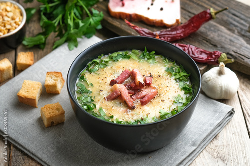 Pea soup with bacon, herbs and bread crumbs in a black bowl on a rustic background.