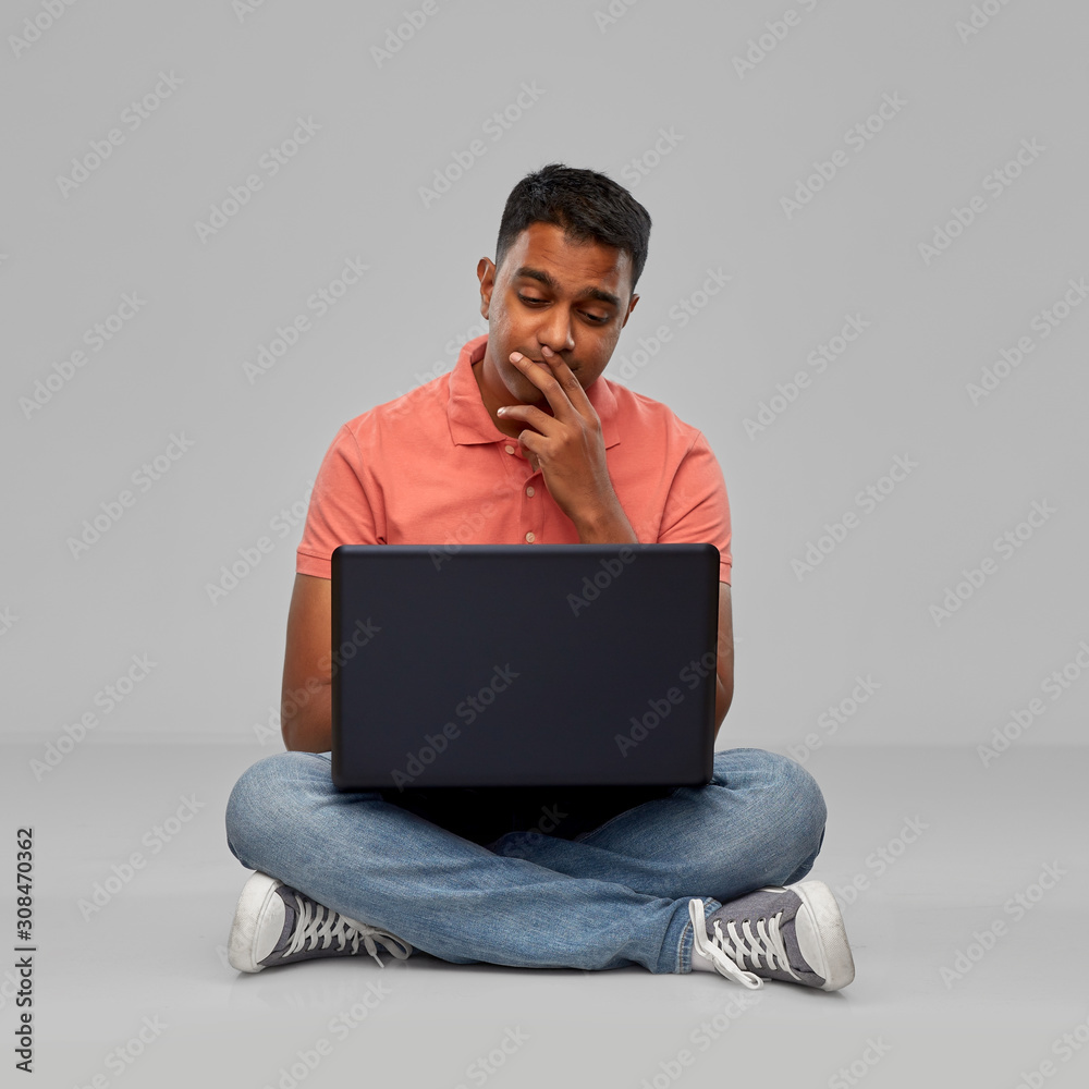 technology, internet, communication and people concept - thinking indian man with laptop computer sitting on floor over grey background technology, internet, communication and people concept - thinking indian man with laptop computer sitting on floor over grey background