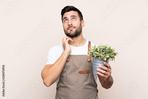 Gardener man holding a plant over isolated background thinking an idea