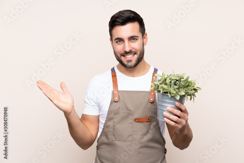 Gardener man holding a plant over isolated background holding copyspace imaginary on the palm