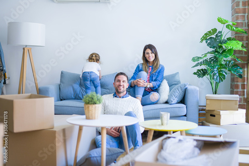 Beautiful family  parents sitting on the sofa looking his kid jumping at new home around cardboard boxes