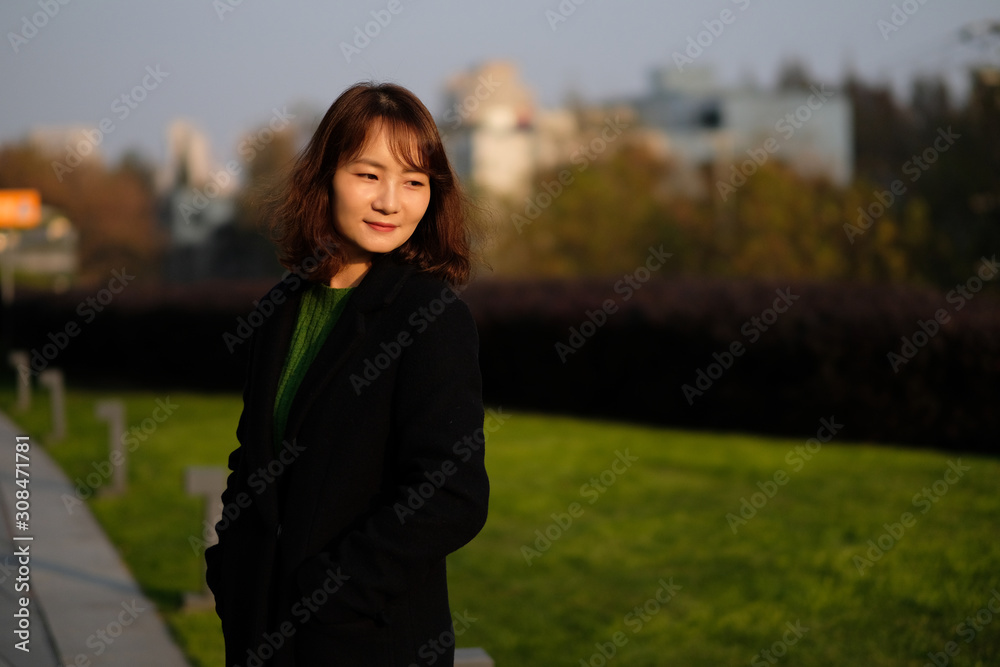 One Asian young woman standing outdoor under sunshine. Blur green grass and city background One Asian young woman standing outdoor under sunshine. Blur green grass and city background