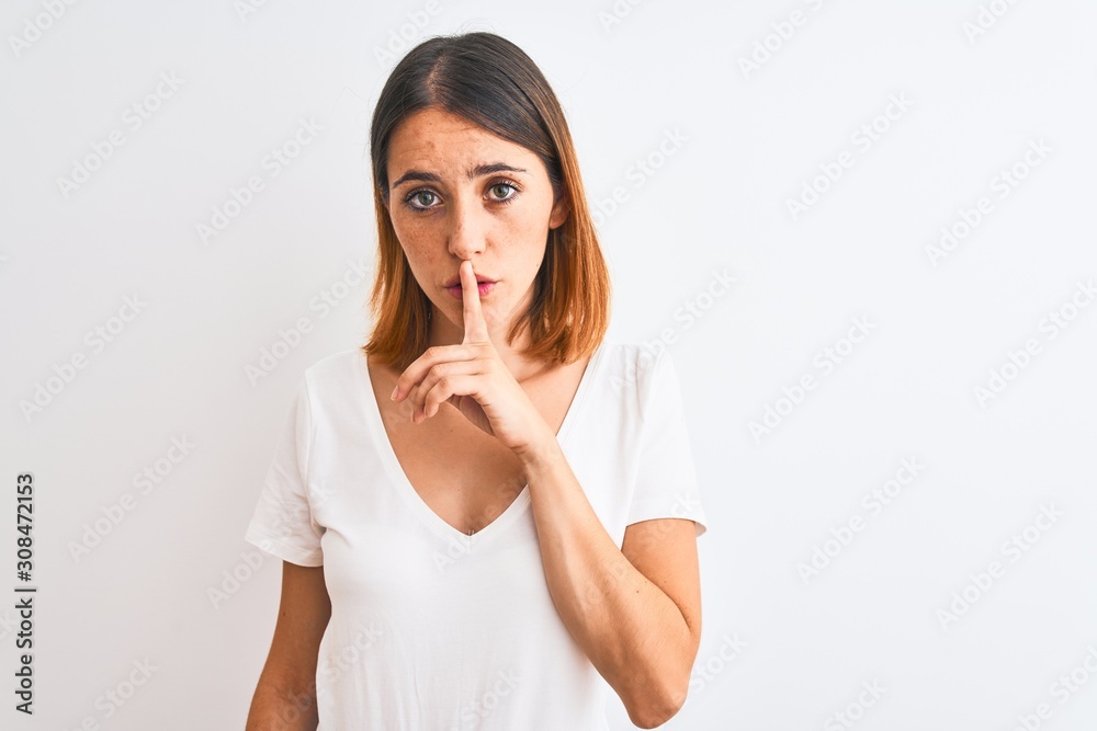 Beautiful redhead woman wearing casual white t-shirt over isolated background asking to be quiet with finger on lips. Silence and secret concept. Beautiful redhead woman wearing casual white t-shirt over isolated background asking to be quiet with finger on lips. Silence and secret concept.