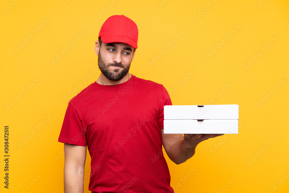 pizza delivery man with work uniform picking up pizza boxes over isolated yellow background with sad expression pizza delivery man with work uniform picking up pizza boxes over isolated yellow background with sad expression