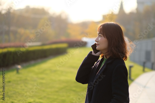 One Asian young woman making phone call outdoor under sunshine. Blur background