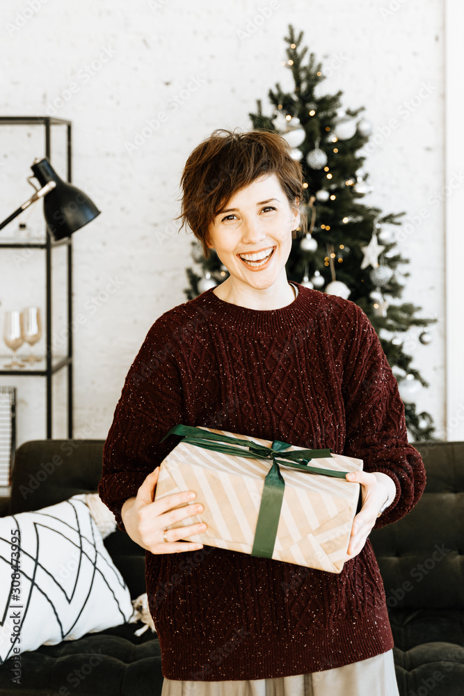 Happy young woman with short hair in sweater unpack Christmas gift at home. Happy young woman with short hair in sweater unpack Christmas gift at home.