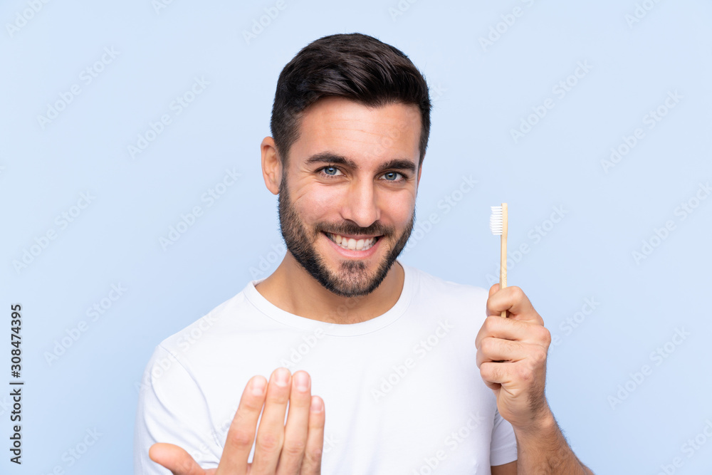 Young handsome man with beard brushing his teeth over isolated background inviting to come with hand. Happy that you came Young handsome man with beard brushing his teeth over isolated background inviting to come with hand. Happy that you came