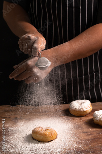 Master Chef's hands sprinkling sugar powder over homemade donut. Selective focus.