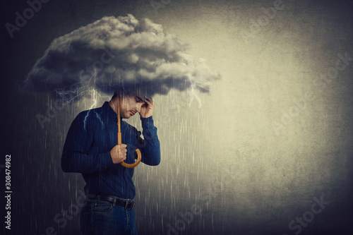 Pessimistic man, standing under rain, suffering anxiety as holding an umbrella thunderstorm cloud over head. Concept of memory loss and dementia disease. Alzheimer's losing brain and memory function.