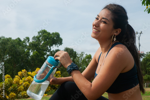Woman with water bottle in the foreground, smiling, background trees