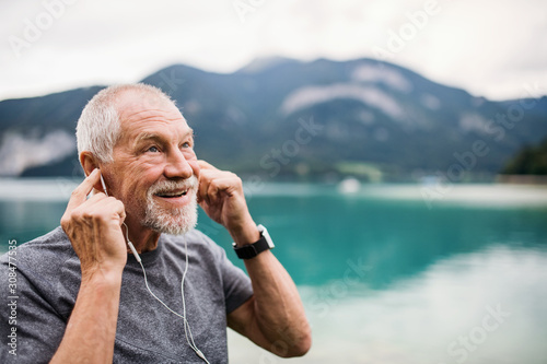 Foto Senior man with earphones standing by lake in nature, listening to music