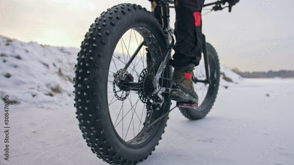 Professional extreme sportsman biker riding fat bike in outdoors. Close-up view of rear wheel. Cyclist ride in winter forest. Man on mountain bicycle with big tire. Snow fly into the lens camera. Professional extreme sportsman biker riding fat bike in outdoors. Close-up view of rear wheel. Cyclist ride in winter forest. Man on mountain bicycle with big tire. Snow fly into the lens camera.