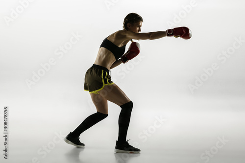 Fit caucasian woman in sportswear boxing isolated on white studio background. Novice female caucasian boxer training and practicing in motion and action. Sport, healthy lifestyle, movement concept. © master1305