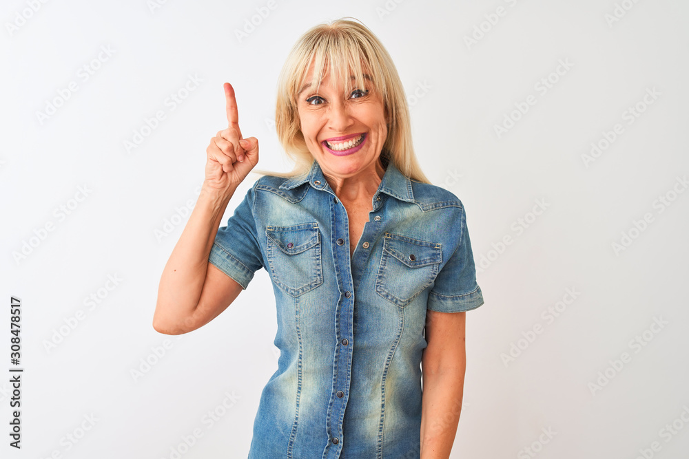Middle age woman wearing casual denim shirt standing over isolated white background pointing finger up with successful idea. Exited and happy. Number one. Middle age woman wearing casual denim shirt standing over isolated white background pointing finger up with successful idea. Exited and happy. Number one.
