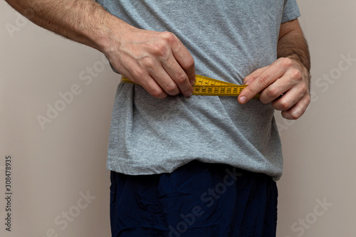 man in a gray T-shirt measures the waist with a yellow tape