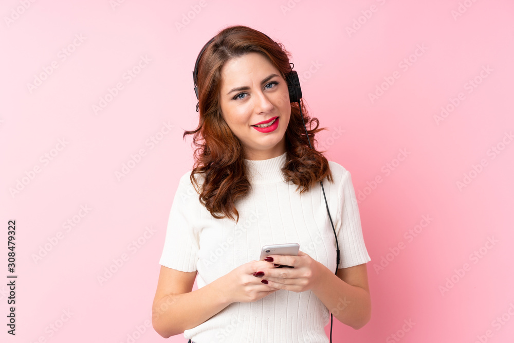 Young Russian woman over isolated pink background using the mobile with headphones Young Russian woman over isolated pink background using the mobile with headphones