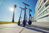 Three black colour electric scooters for adults outdoors on blue sky tropical climate landscape background, no people. Modern technology land vehicle eco alternative transport concept