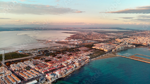 Aerial distant top eye bird view Salt Lake heap of salt and calm turquoise Mediterranean Sea, Torrevieja cityscape between of waters landscape during sunset. Province of Alicante, Costa Blanca, Spain