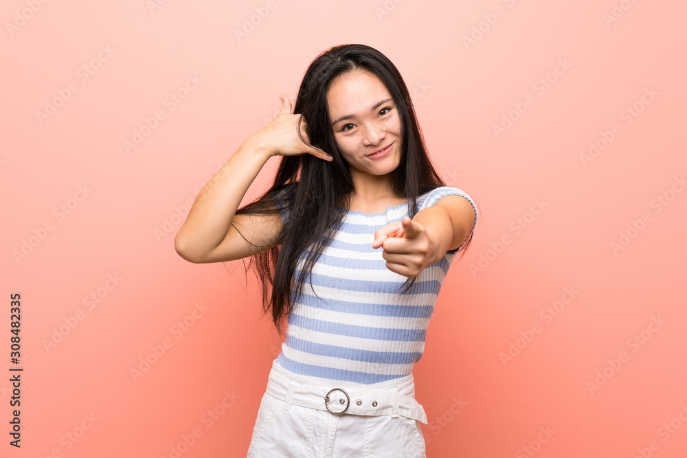 Teenager asian girl over isolated pink background making phone gesture and pointing front Teenager asian girl over isolated pink background making phone gesture and pointing front