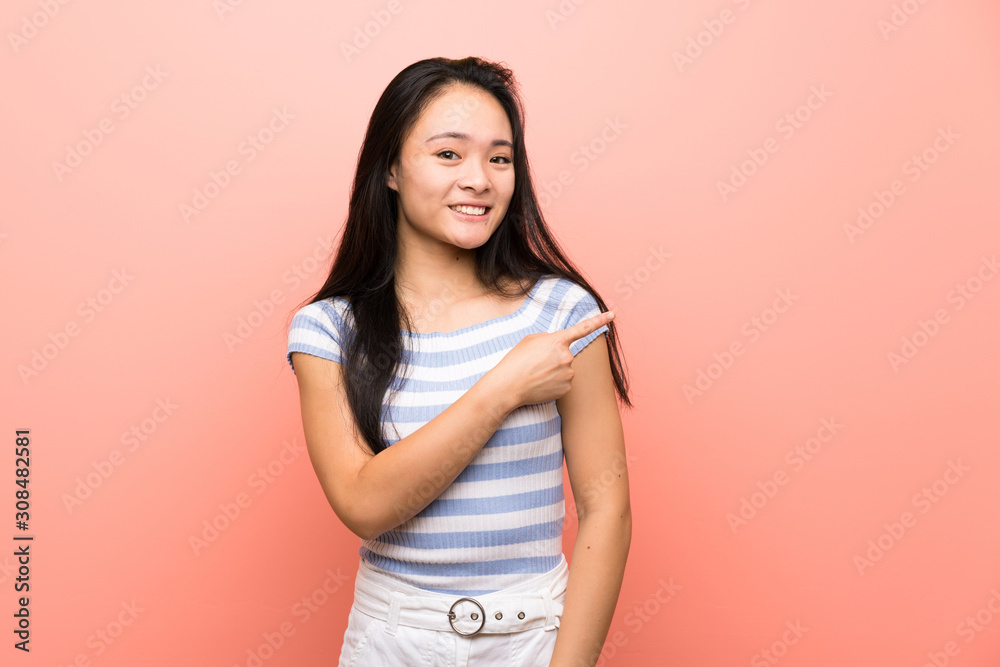 Obraz premium Teenager asian girl over isolated pink background pointing to the side to present a product