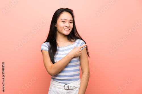 Teenager asian girl over isolated pink background pointing to the side to present a product