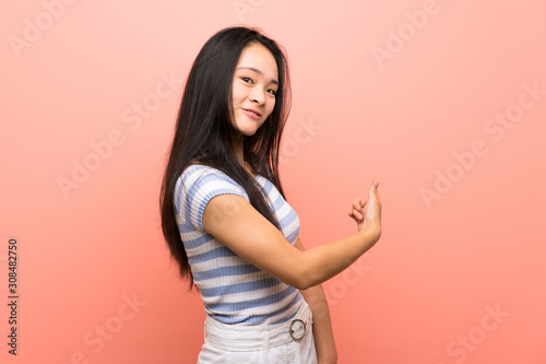 Teenager asian girl over isolated pink background pointing back