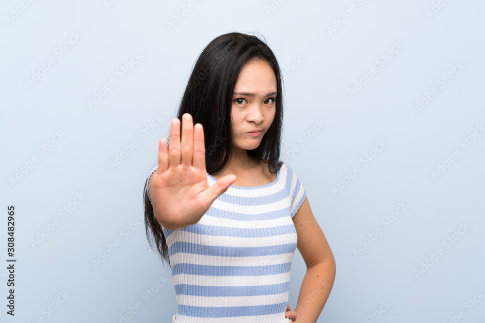 Teenager asian girl over isolated blue background making stop gesture with her hand Teenager asian girl over isolated blue background making stop gesture with her hand